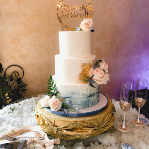 Buttercream cake with blue watercolor on the bottom, gold leaf and real flowers
