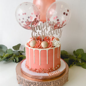 Rose gold buttercream with white drip, sprinkles, cake balls and balloons