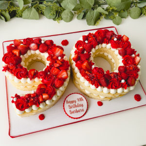 Cake in the shape of a 90 with red fruits and buttercream on top