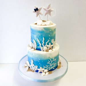 Blue and white buttercream cake with white beach themed decorations and a starfish bride and groom on top