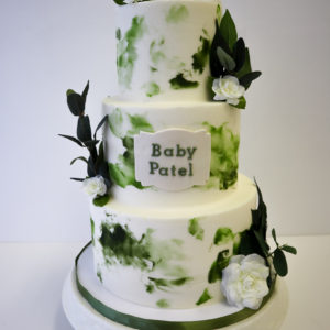 An abstract buttercream cake with greenery and baby booties on top.
