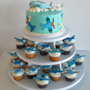 A small cake with a plane carrying a "It's a Boy" banner and cupcakes to match