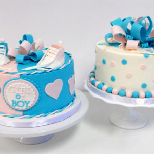 Two gender reveal cakes with edible bows and baby shoes
