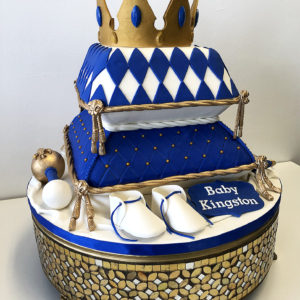Navy and white pillow cake with gold accents, gold crown on top and fondant baby booties.