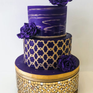 Purple and gold marble cake with gold flower pattern and purple sugar flowers.