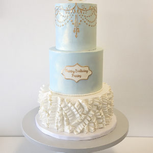 Fondant cake with fondant white ruffles on the bottom and gold royal icing chandelier stencil on top