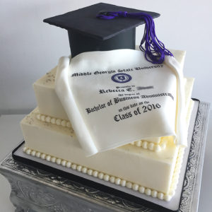 A simple two tiered square cake with edible hat and diploma on top