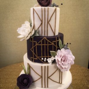 A white and purple fondant cake with gold geometric detail and sugar flowers