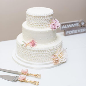 A three tier buttercream cake with buttercream ruffles and Swiss dots. The flowers are gumpaste dusted with petal dust.