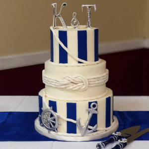 Fondant cake with navy stripes and fondant rope infinity knot. Accented with silver fondant molded anchor and captains wheel.