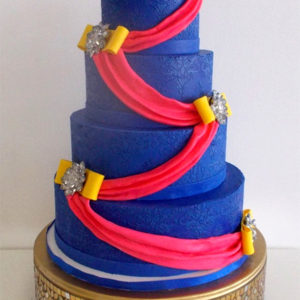 Blue cake with royal icing stenciled pattern in the same color with a bright pink drape to match the bride's sari
