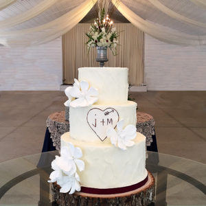 Rustic buttercream cake with sugar magnolias and fondant painted heart in the middle.