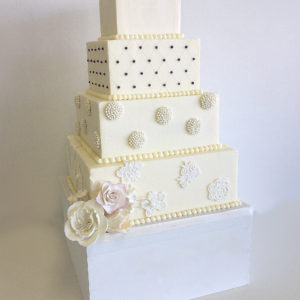 Four tiered square buttercream cake with a quilted pattern, pearl broaches and embossed fondant lace pieces.