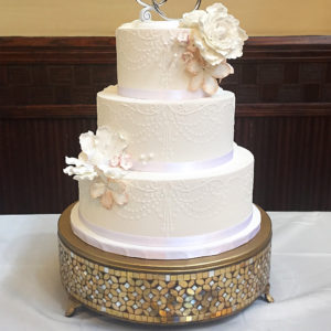 Three tiered fondant cake with a chandelier designed stenciled with royal icing in the front and sugar flowers.